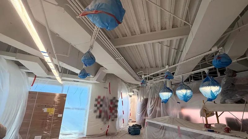 Exposed ceiling with fixtures bagged in blue plastic and walls covered in sheeting before painting