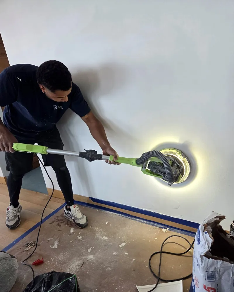 Crew member sanding a wall smooth with a dust-collecting sander