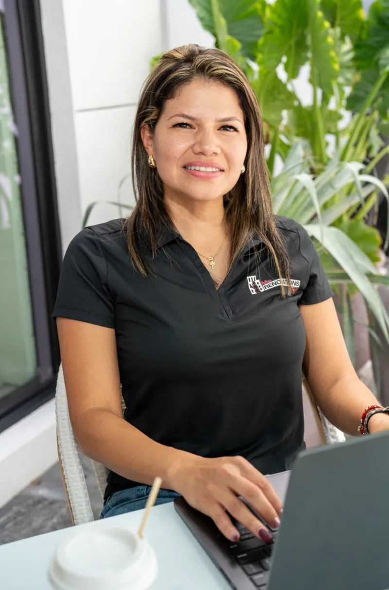 The owner of Ms Renovations Pro seated at a laptop, smiling, in a company polo